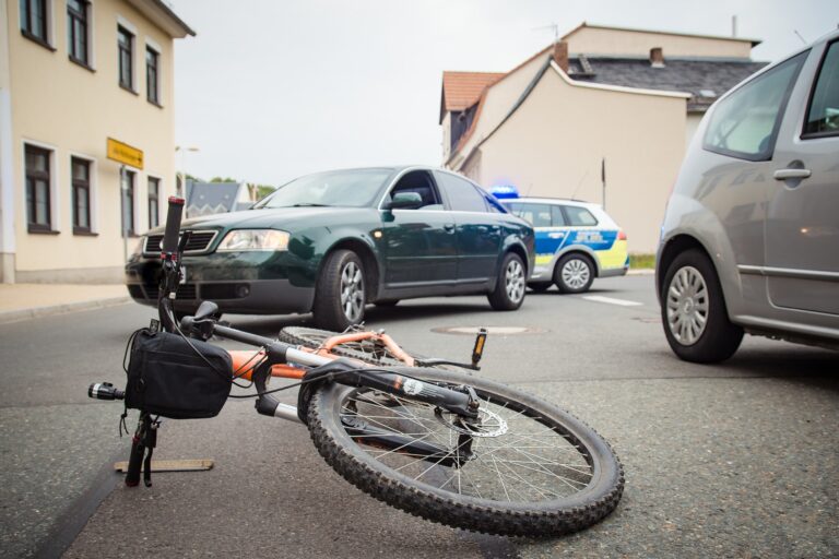 Bicycle lying on the ground with visible damage, and a car with dents in the background, illustrating a collision scenario